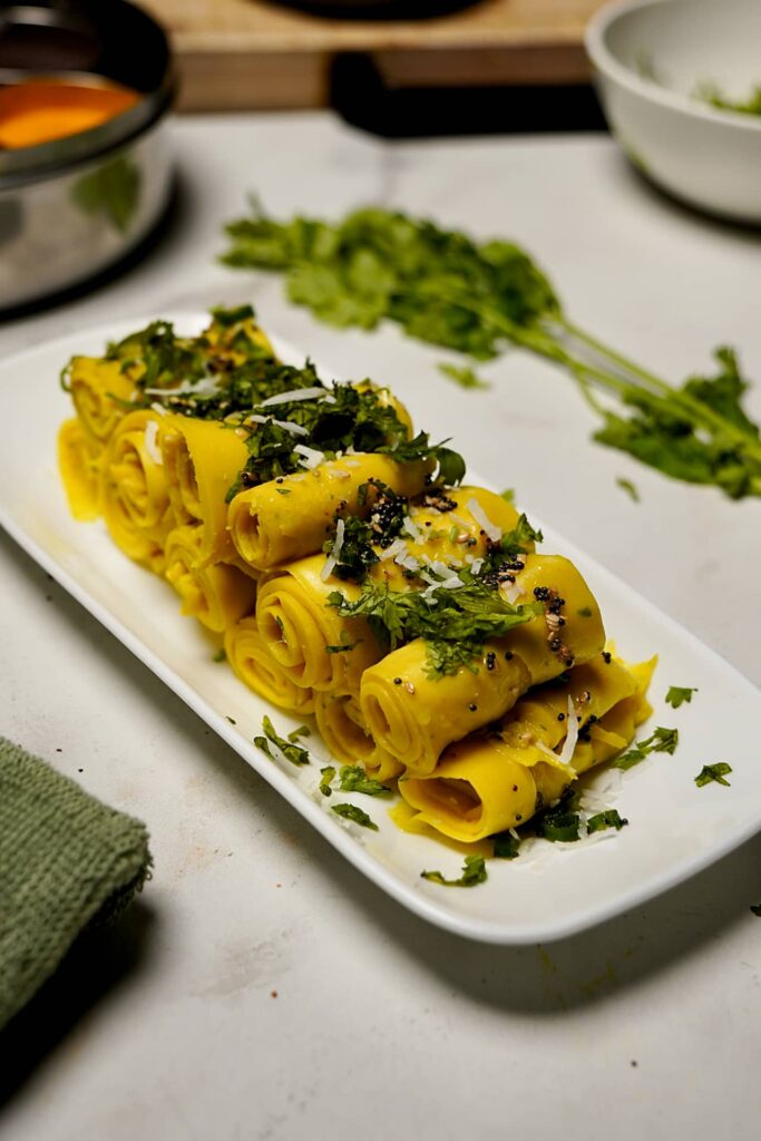 Sliced Khandvi arranged neatly on a plate, highlighting its spiral shape.